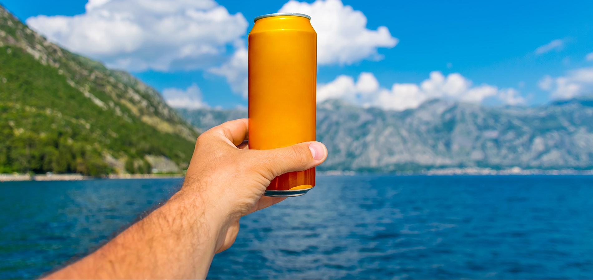 Orange can being held up against a background with a lake and mountains.