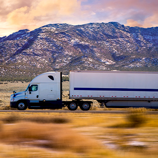 A semi-truck driving on the road in front of mountains.